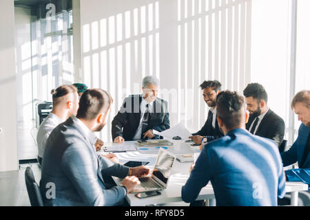 Multiracial male business executives discuss project sitting at conference table Stock Photo