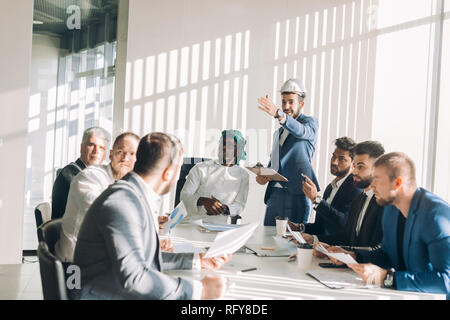 Multiracial male business executives discuss project sitting at conference table Stock Photo