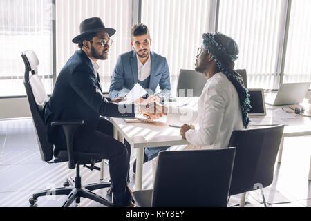 Sealing a deal. Top view of three men sitting at the desk and shaking hands Stock Photo