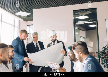 Multiracial group of constructors and architects discussing blueprint at office. Stock Photo