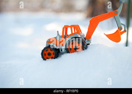 Orange toy tractor with large black wheels close-up, standing in the snow. Stock Photo