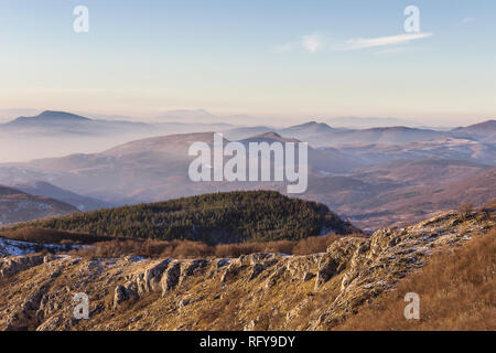 Misty mountain layers, distant Rtanj summit, sunlit foreground rocks and pine tree forest Stock Photo