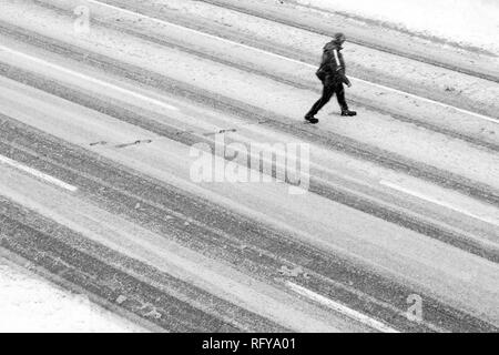 One man crossing the empty street during the snowstorm, high angle view in black and white Stock Photo