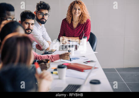 Mixed race people listening to presentation sitting in row at boardroom table Stock Photo