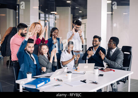 Young multi-ethnic work team exchanges ideas gathering around laptop computers Stock Photo