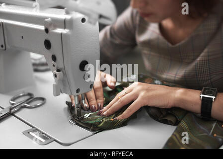Woman seamstress working on modern electrical sewing machine connecting colorful clothing details. Dressmaker making garment in studio. Hobby, do it y Stock Photo