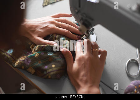 Close-up of female seamstress hands sewing clothing detail on electrical sewing machine. Tailor atelier - handmade exclusive clothes making and repair Stock Photo