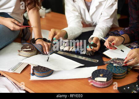Fashion designers female team working on clothes creation, choosing accessories, buttons and details for new collection, discussing sketches. Teamwork Stock Photo