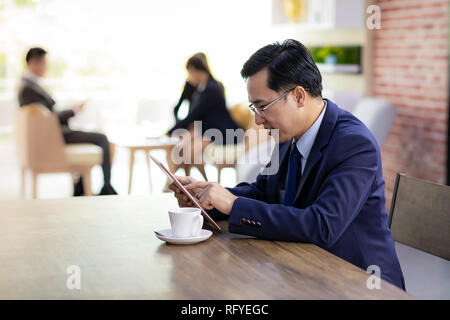 Portrait of Businessman working in cafe using smart phone tablet with business team in background using for coporate background work Stock Photo