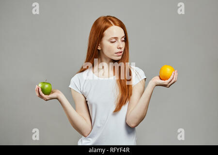 red haired caucasian woman comparing apples and oranges. Stock Photo