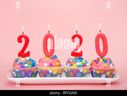 White cupcakes with rainbow colored frosting and brightly colored star candies on a rectangular plate pink background with 2020 candles burning. Happy Stock Photo