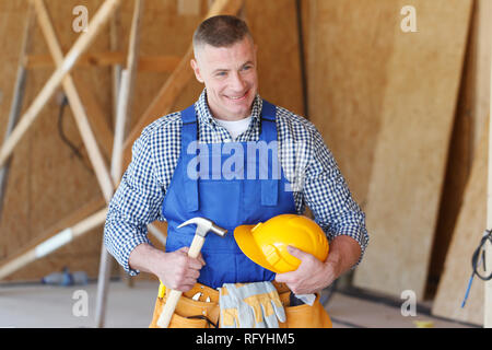 Construction worker at construction site holding hammer and hardhat Stock Photo