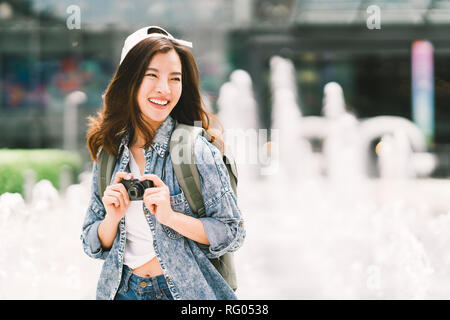 Young beautiful Asian backpack traveler woman using digital compact camera and smile, looking at copy space. Journey trip lifestyle, world travel Stock Photo