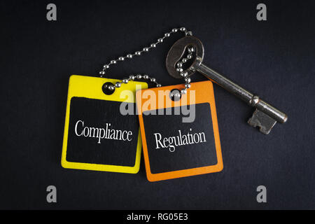 COMPLIANCE REGULATION inscription written on wooden tag and key on black background with selective focus and crop fragment. Business and education con Stock Photo