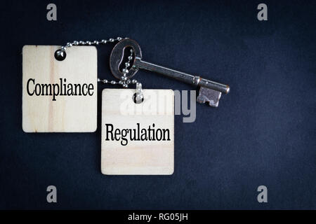 COMPLIANCE REGULATION inscription written on wooden tag and key on black background with selective focus and crop fragment. Business and education con Stock Photo