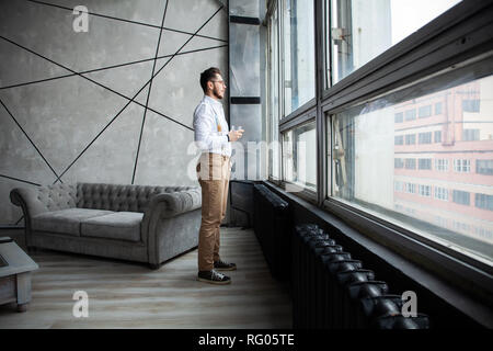 Success concept. Stylish young bearded man is standing near the window and looking far. He is in a suit, pensive and concentrated. Stock Photo