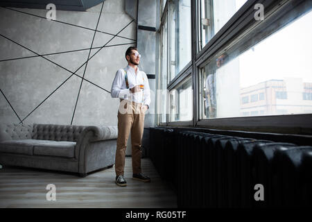 Success concept. Stylish young bearded man is standing near the window and looking far. He is in a suit, pensive and concentrated. Stock Photo