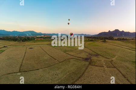 Aerial: Vang Vieng backpacker travel destination in Laos, Asia. Sunset over scenic cliffs and rock pinnacles, rice paddies valley, hot air balloons. Stock Photo