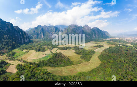 Aerial: Vang Vieng backpacker travel destination in Laos, Asia. Dramatic sky over scenic cliffs and rock pinnacles, rice paddies valley, stunning land Stock Photo