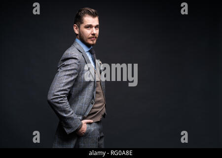 A confident elegant handsome young man standing in front of a black background in a studio wearing a nice suit. Stock Photo