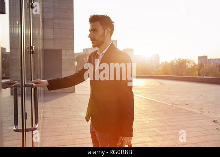 Men's fashion. A young male businessman in a trendy suit and a white shirt with a big black handbag comes out from a fashionable clothing store. Outdo Stock Photo