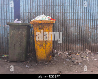 Plastic waste full of garbage bin dirty green and yellow on dirty light blue of wall. Stock Photo