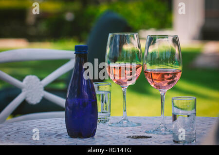Two glasses with rose wine and blue bottle of water on the table in the garden Stock Photo