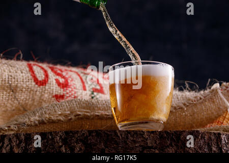 Light beer pours into a glass goblet standing on a wooden saw. Close-up. Stock Photo