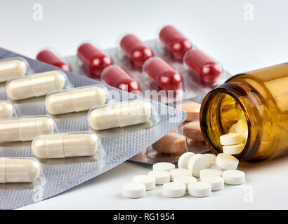 Close-up view of colorful pills and drugs spilled from a brown medicine bottle on a blurred white background Stock Photo