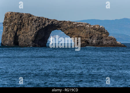 Small sailboat is visible through the Anacapa Island Arch on a sunny winter day in the Channel Islands National Park off the Pacific Ocean coast of Ve Stock Photo