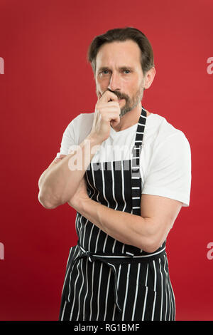 Concentrated on the task. Doing household. Bearded mature man in striped apron. Senior cook wearing bib apron. Mature person in cooking apron. Aged master of the household. Home cooking. Stock Photo