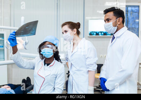 Health and healthcare. A multinational group of dentists examines x-rays in the presence of a patient. Practice at a medical university. Dental clinic Stock Photo