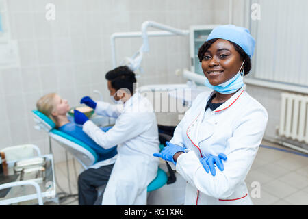 Portrait of Female black dentist in dental office. She standing at her office and she has beautiful smile. Modern medical equipment Stock Photo