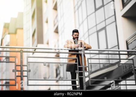 Indian young man in glasses use phone stands on the background of buildings Stock Photo
