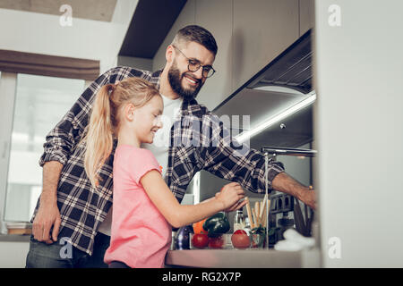 Little girl and her tall bearded father in eyeglasses spending time in the kitchen Stock Photo