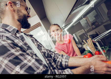 Cute long-haired girl in a pink t-shirt looking attentively to her father Stock Photo