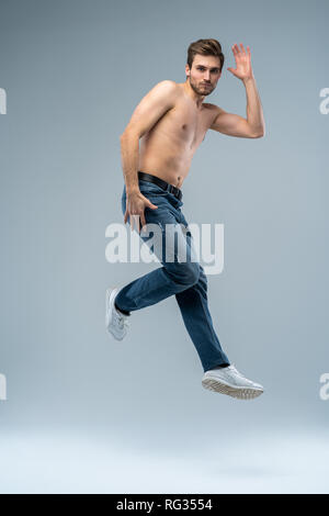 Full-length photo of funny man running or jumping in air isolated over gray background. Stock Photo