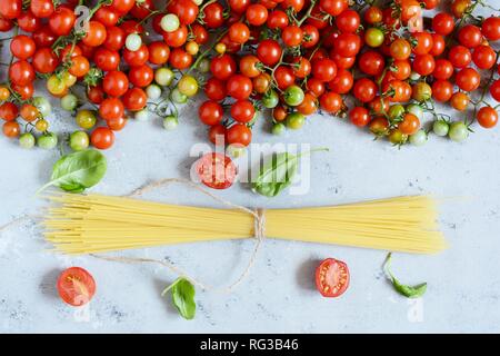 Food frame. Pasta ingredients concept. Uncooked spaghetti and cherry tomato with green basil on a blue background. Top view with copy space. Italian f Stock Photo