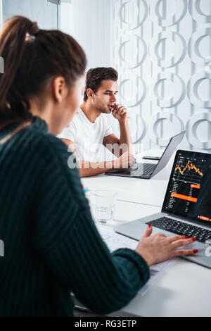 Two business colleagues working together at modern office and using laptop. Young coworking people team sitting at table and having meeting about new  Stock Photo