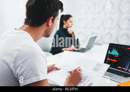 Concentrated building designers working with drawing plan and computer while sitting by the table at studio office. Young team of architect using lapt Stock Photo