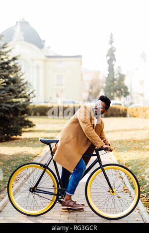 Young bearded indian man in coat while sitting on his bicycle outdoors Stock Photo