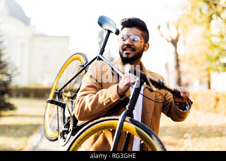 Bearded indian man carrying bicycle on shoulder in the city Stock Photo