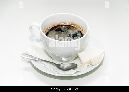 A Cup of black coffee on a saucer with a napkin, a teaspoon and pieces of sugar on a white background Stock Photo