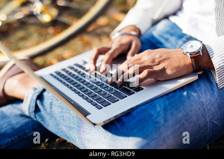 Close up working on laptop on grass with bicycle and laptop in park Stock Photo