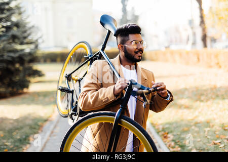 Bearded indian man carrying bicycle on shoulder in the city Stock Photo