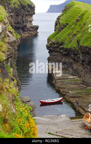 A small red boat sits in the water between two tall cliffs Stock Photo