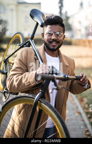 Young asian cheerful businessman holding bike on shoulder in outdoor city. Happy success business man cycling go to work with bike in city Stock Photo