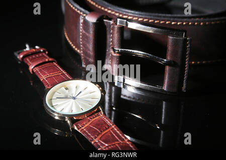 Men's accessories for business and rekreation. Leather belt, Watch, notepad and pen on black mirror background. Top view composition Stock Photo