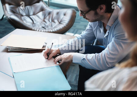 Hispanic Manager Signing Document With Secretary In Business Office Stock Photo