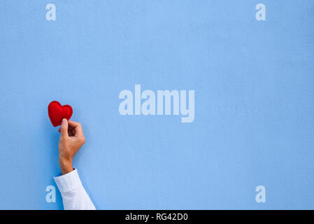 Red Valentine heart in a man's hand on blue wall background. Greeting card with copy space for text Stock Photo
